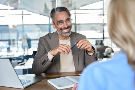 Happy middle aged professional business man executive hr or bank manager, lawyer or financial advisor having job interview or business conversation consulting client at corporate office meeting.